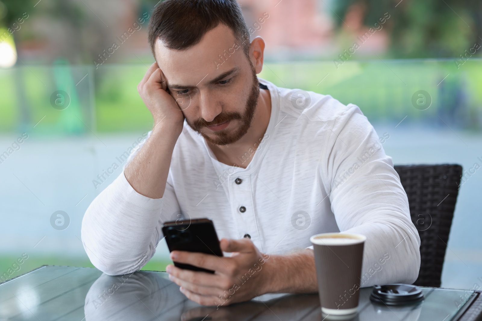 Photo of Handsome man with paper cup using smartphone at outdoor cafe