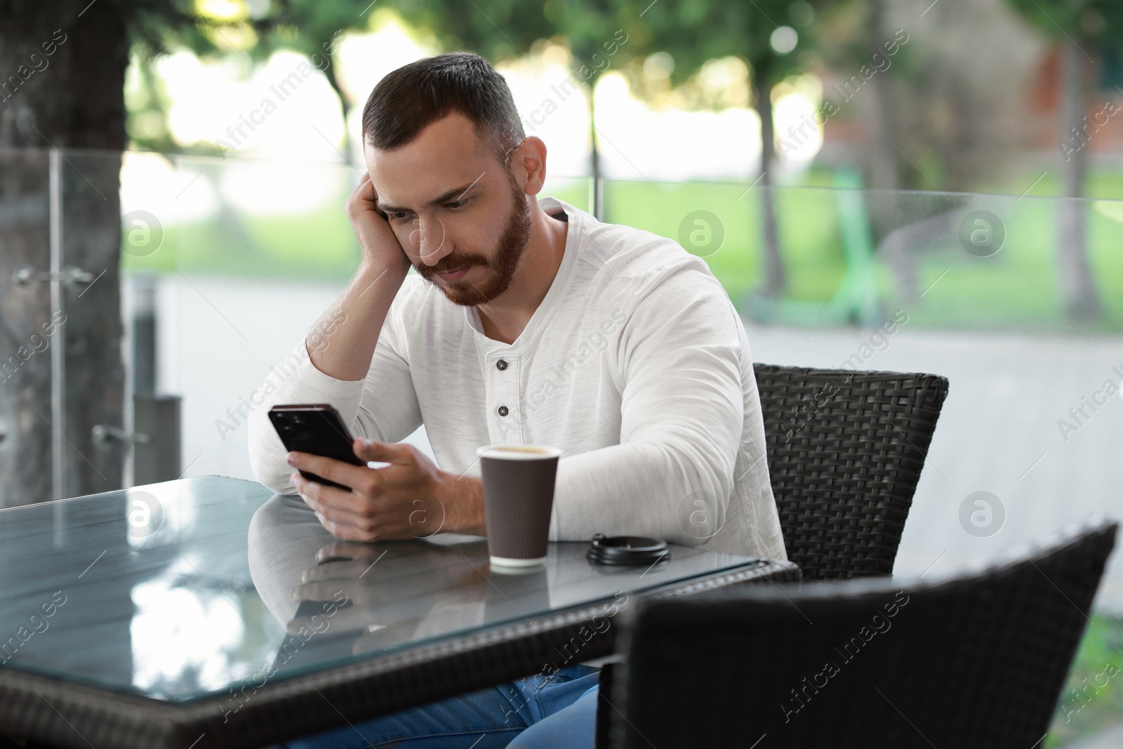 Photo of Handsome man with paper cup using smartphone at outdoor cafe