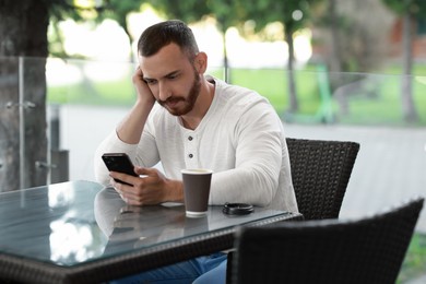 Handsome man with paper cup using smartphone at outdoor cafe