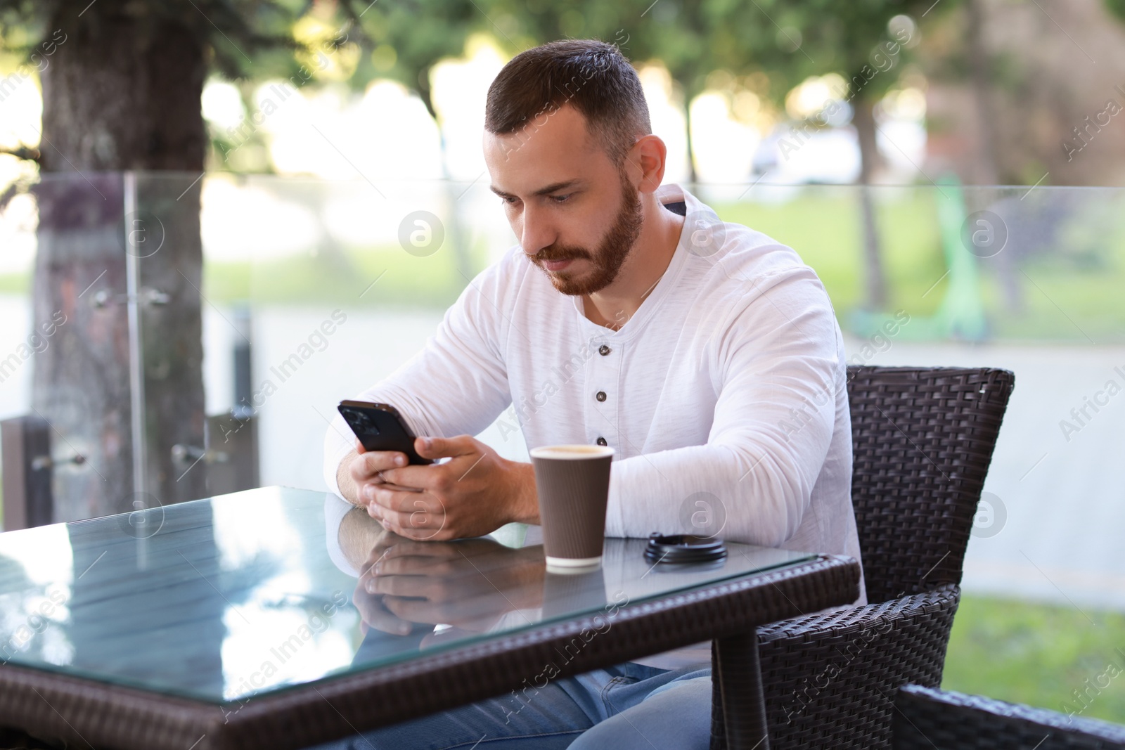 Photo of Handsome man with paper cup using smartphone at outdoor cafe