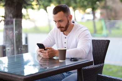 Handsome man with paper cup using smartphone at outdoor cafe