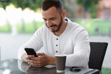 Happy man with paper cup using smartphone at outdoor cafe