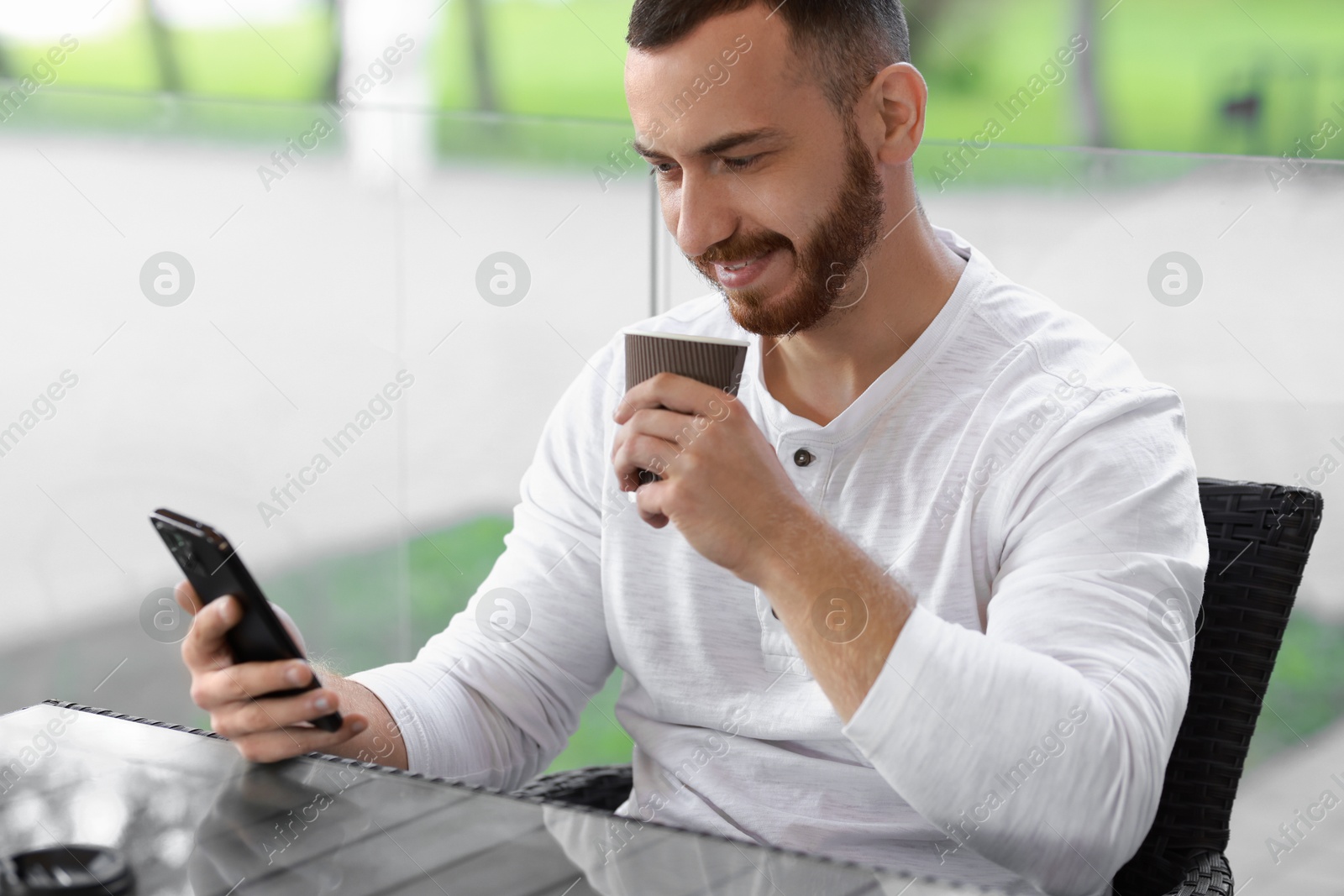 Photo of Handsome man using smartphone and drinking coffee at outdoor cafe