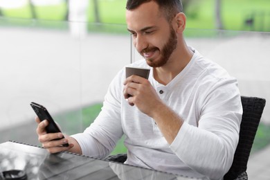 Handsome man using smartphone and drinking coffee at outdoor cafe