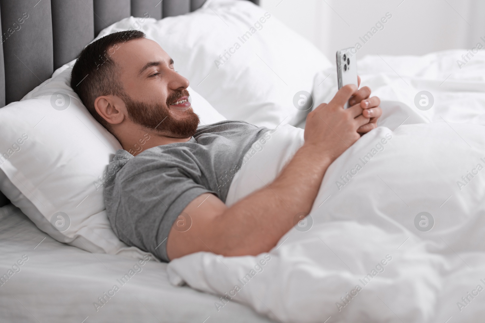 Photo of Smiling man using mobile phone in bed