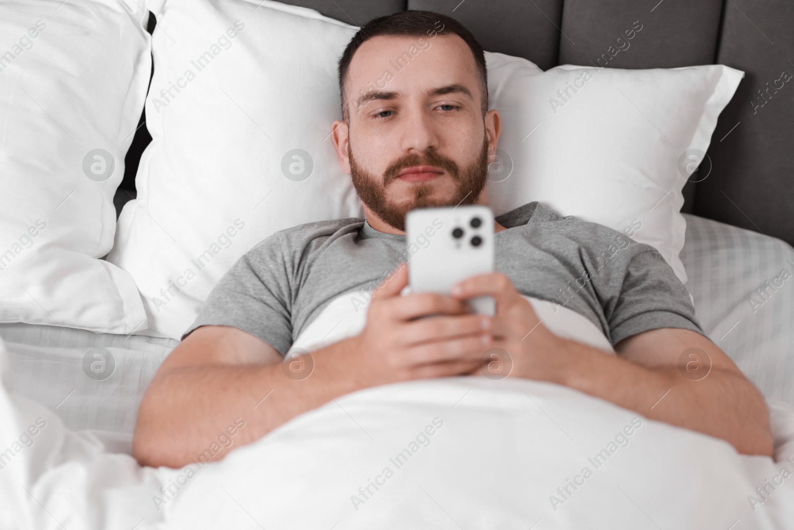 Photo of Handsome man using mobile phone in bed