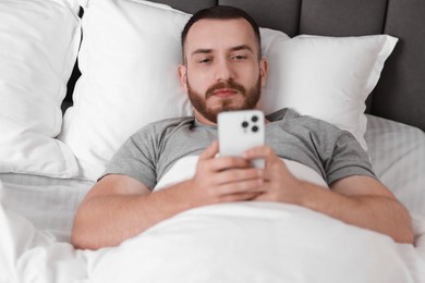 Handsome man using mobile phone in bed