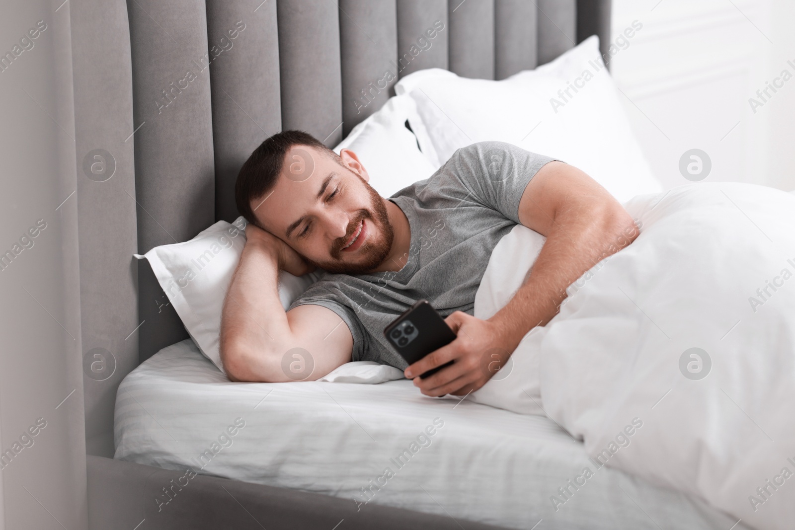 Photo of Smiling man using mobile phone in bed