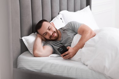 Smiling man using mobile phone in bed