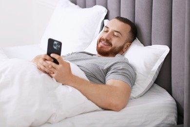 Photo of Smiling man using mobile phone in bed