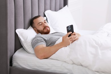 Handsome man using mobile phone in bed