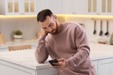 Handsome man looking at smartphone in kitchen