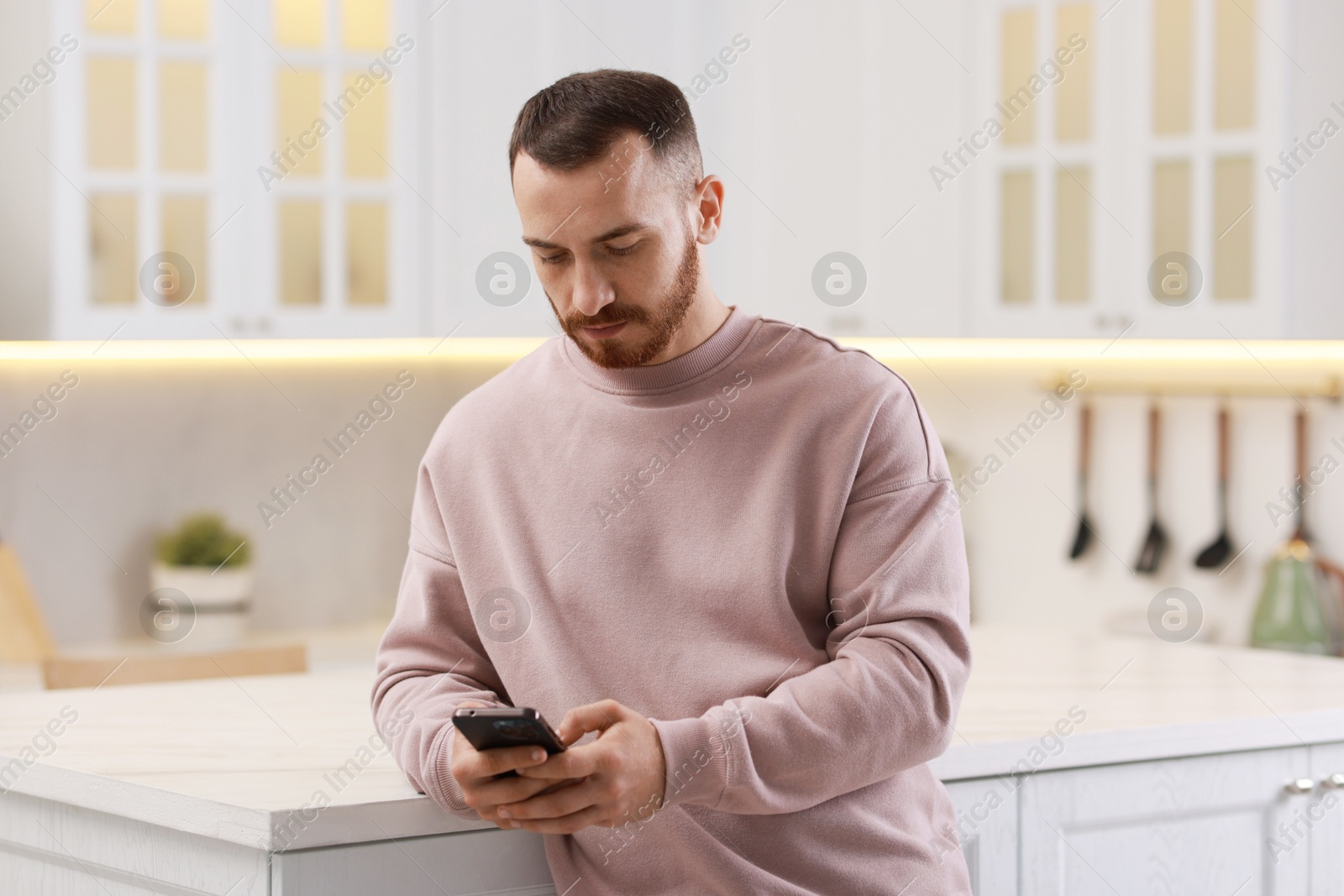 Photo of Handsome man looking at smartphone in kitchen