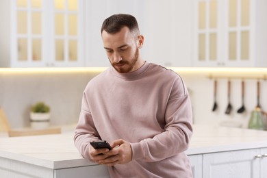 Photo of Handsome man looking at smartphone in kitchen