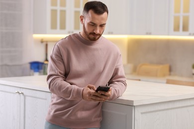 Handsome man looking at smartphone in kitchen