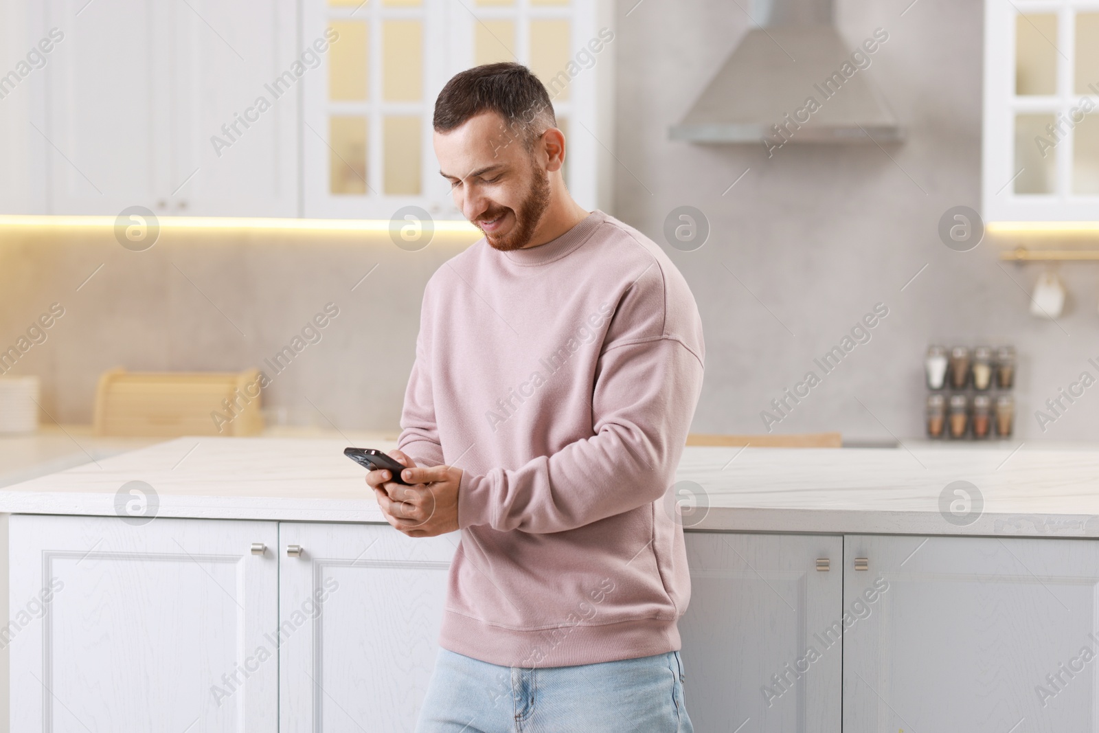 Photo of Happy man looking at smartphone in kitchen