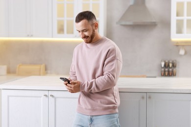 Photo of Happy man looking at smartphone in kitchen