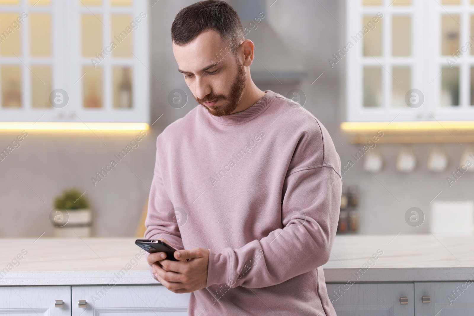 Photo of Handsome man looking at smartphone in kitchen