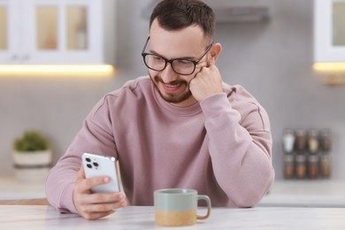 Photo of Happy man using smartphone at white table in kitchen