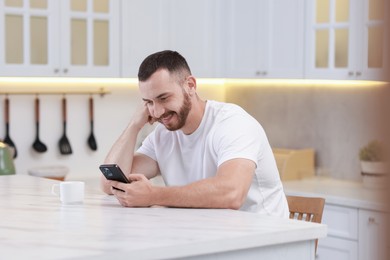 Happy man looking at smartphone in kitchen