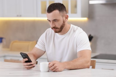 Photo of Handsome man using smartphone at white table in kitchen