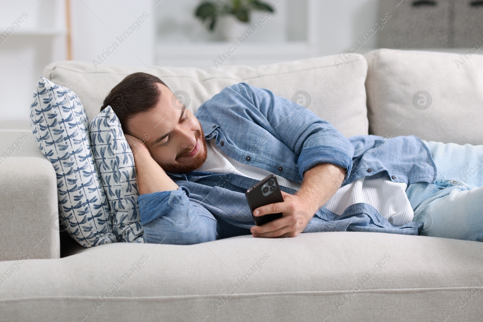 Photo of Handsome man looking at smartphone on sofa indoors