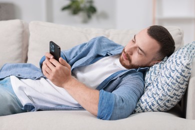 Handsome man looking at smartphone on sofa indoors