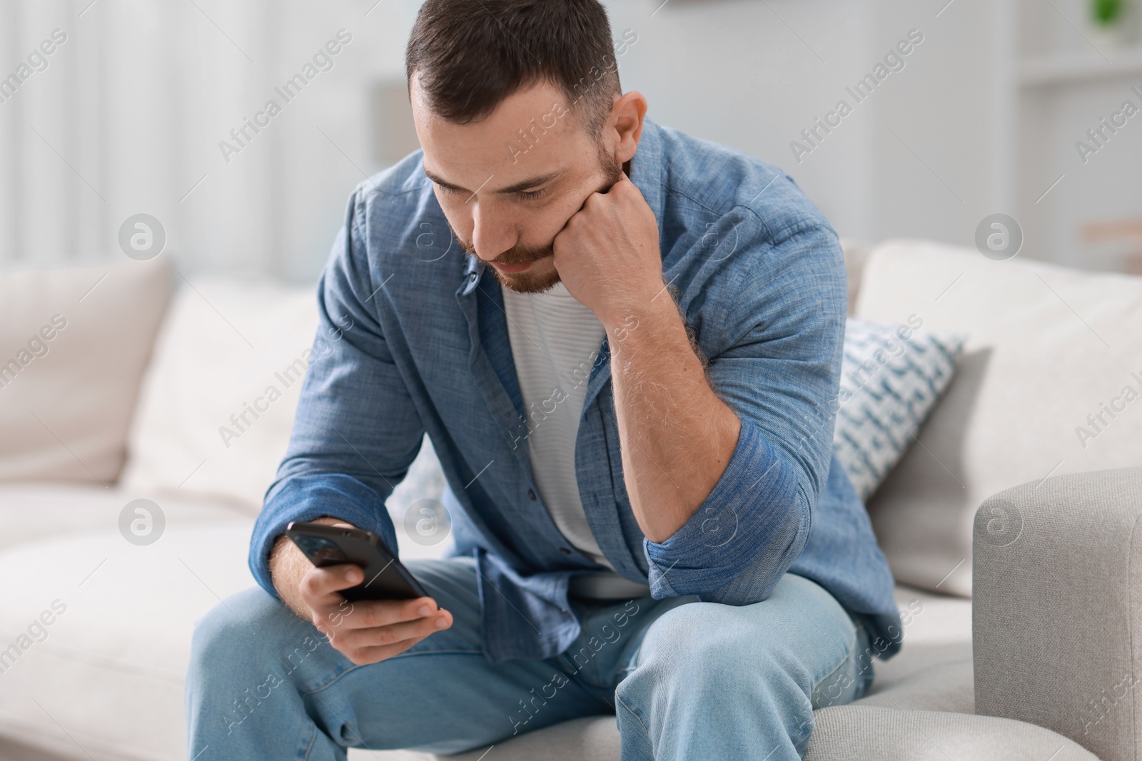 Photo of Handsome man looking at smartphone on sofa indoors