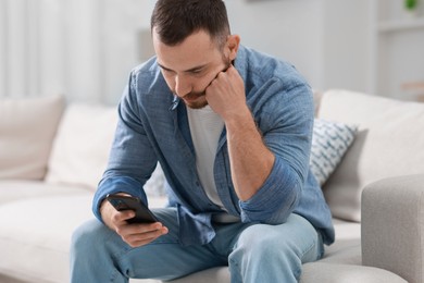 Photo of Handsome man looking at smartphone on sofa indoors