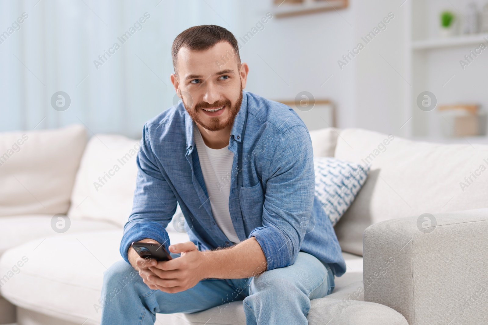 Photo of Smiling man with smartphone on sofa at home