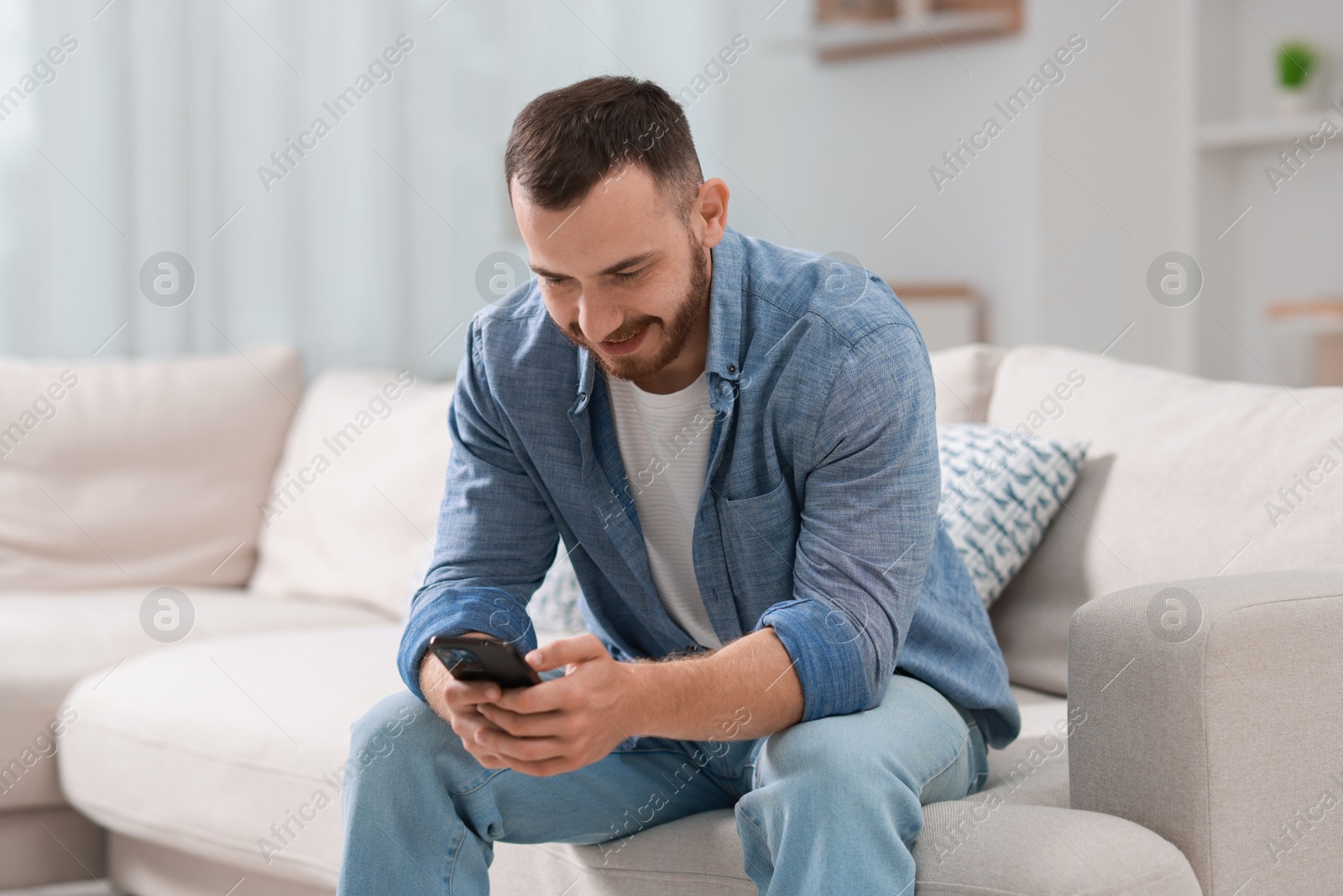 Photo of Handsome man using smartphone on sofa indoors