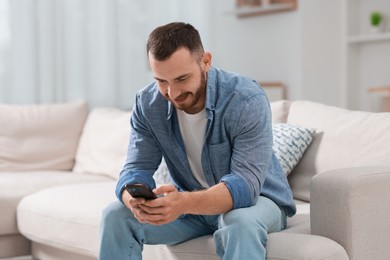 Photo of Handsome man using smartphone on sofa indoors