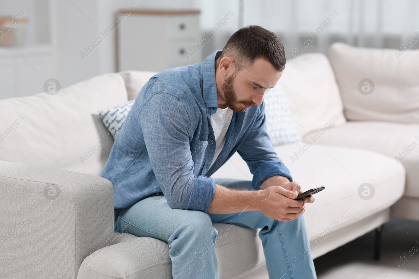 Photo of Handsome man using smartphone on sofa indoors