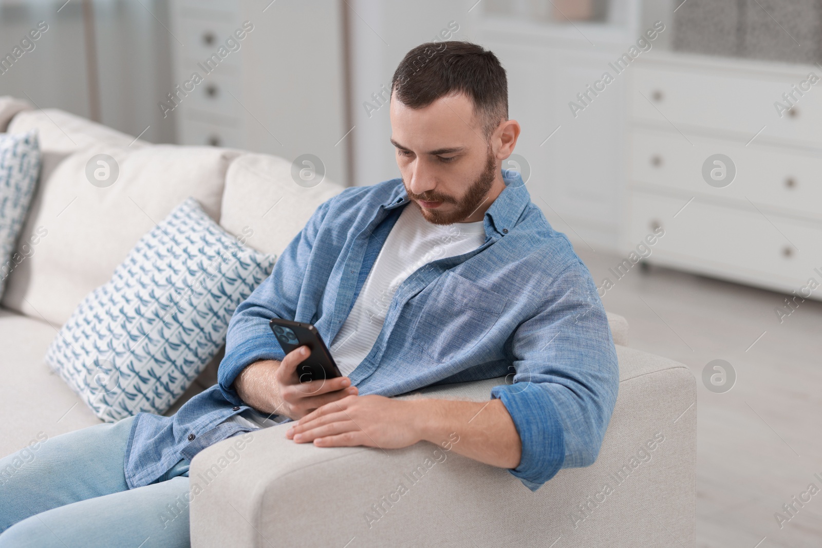 Photo of Handsome man using smartphone on sofa indoors