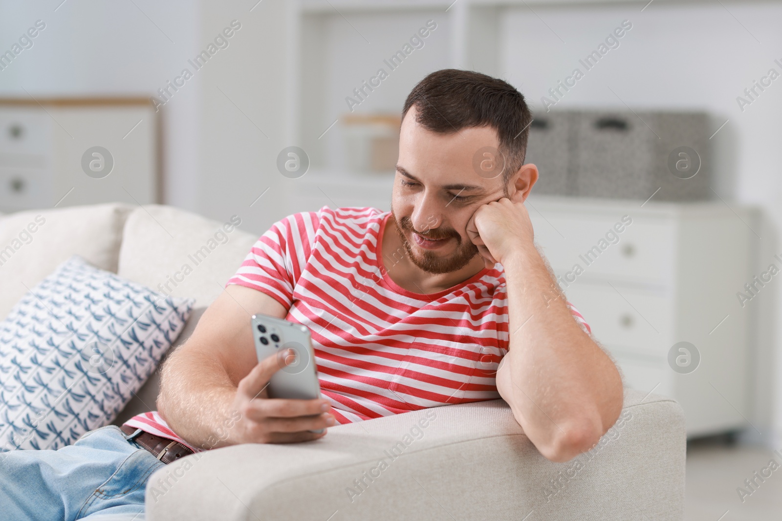 Photo of Handsome man using smartphone on sofa indoors