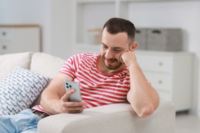 Photo of Handsome man using smartphone on sofa indoors