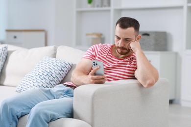 Handsome man using smartphone on sofa indoors