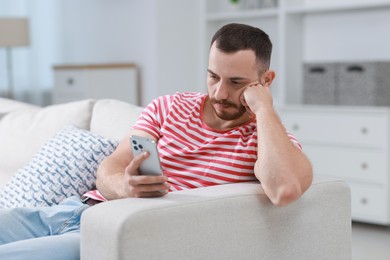 Photo of Handsome man using smartphone on sofa indoors