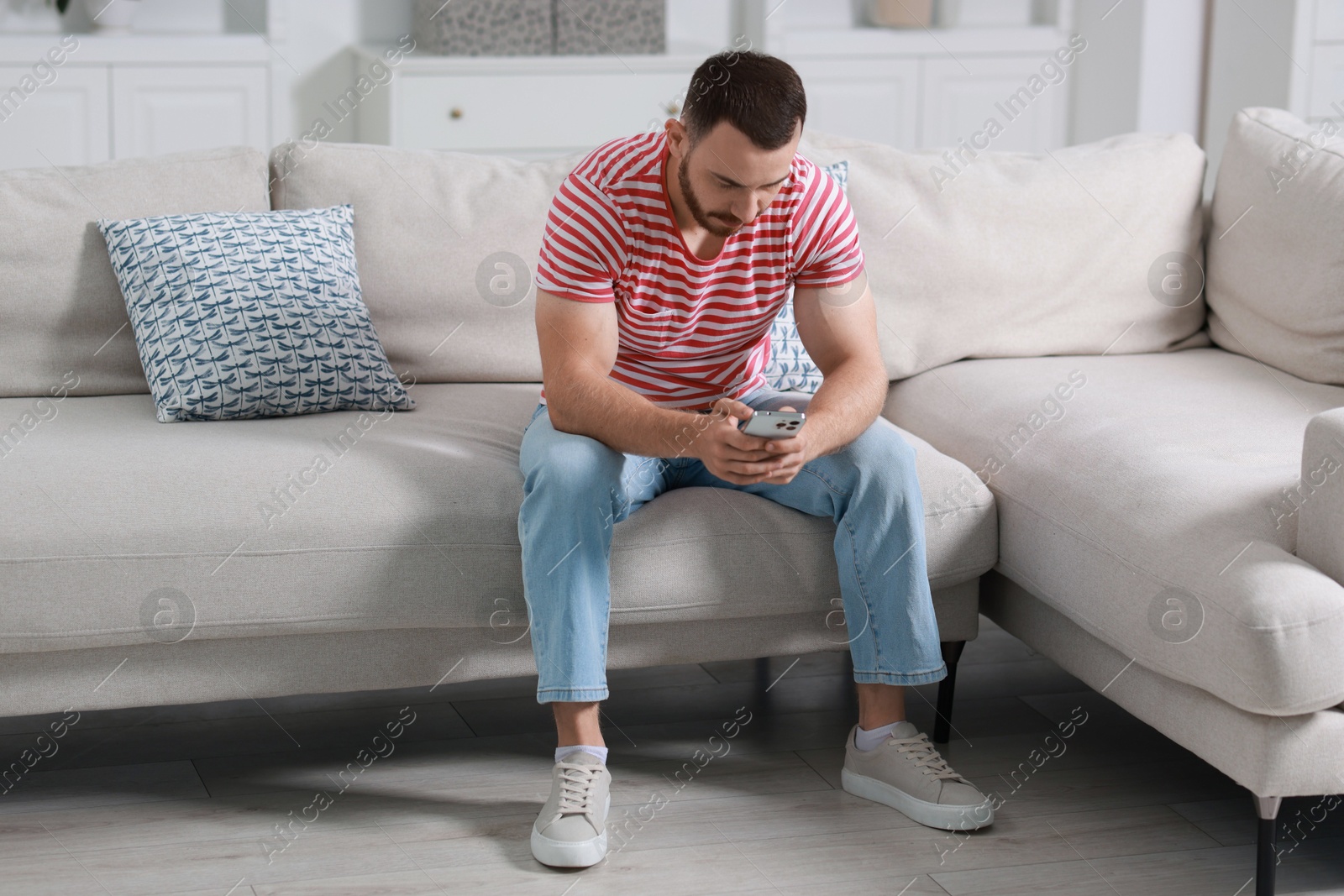 Photo of Handsome man using smartphone on sofa indoors