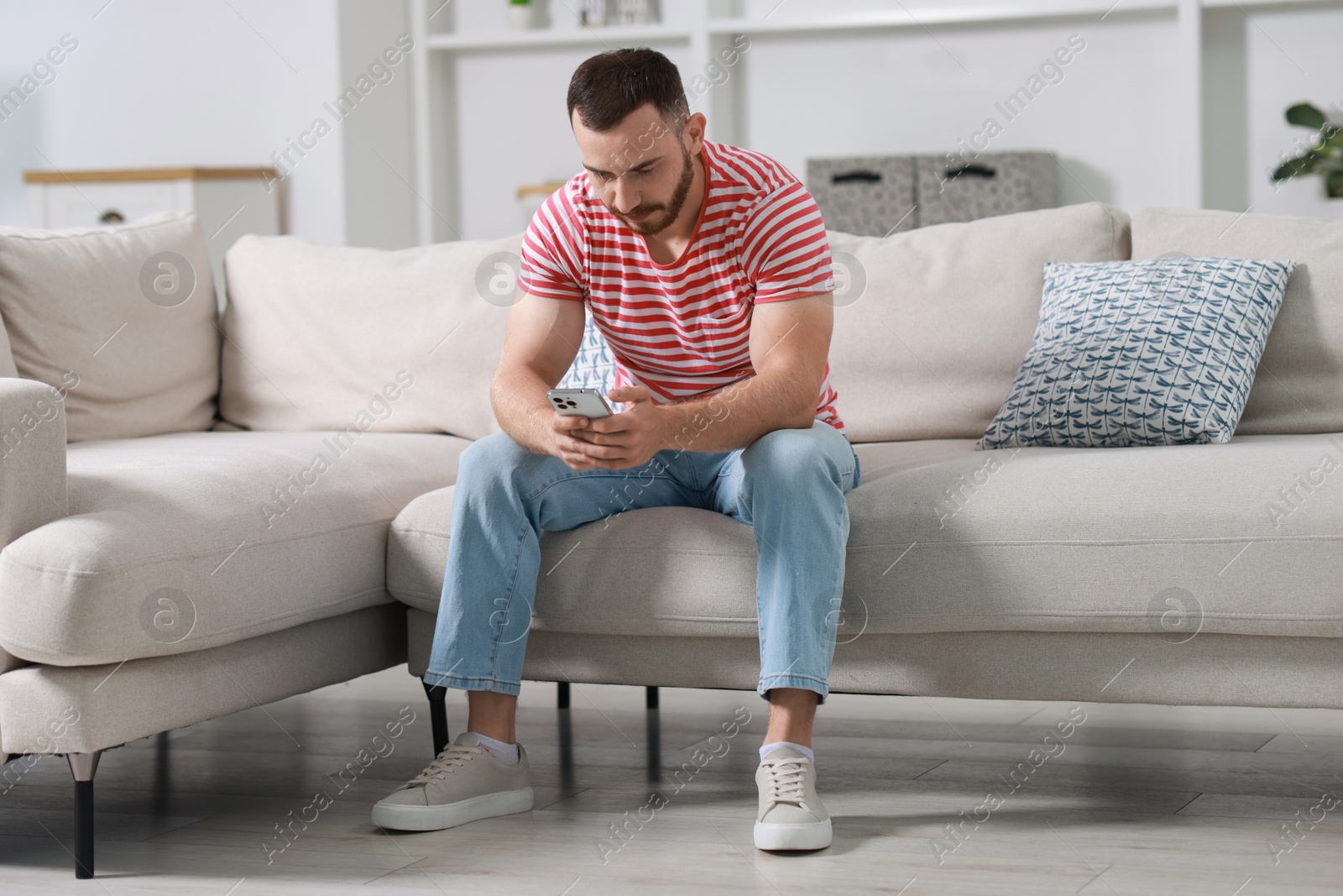 Photo of Handsome man using smartphone on sofa indoors