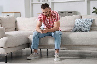 Photo of Handsome man using smartphone on sofa indoors