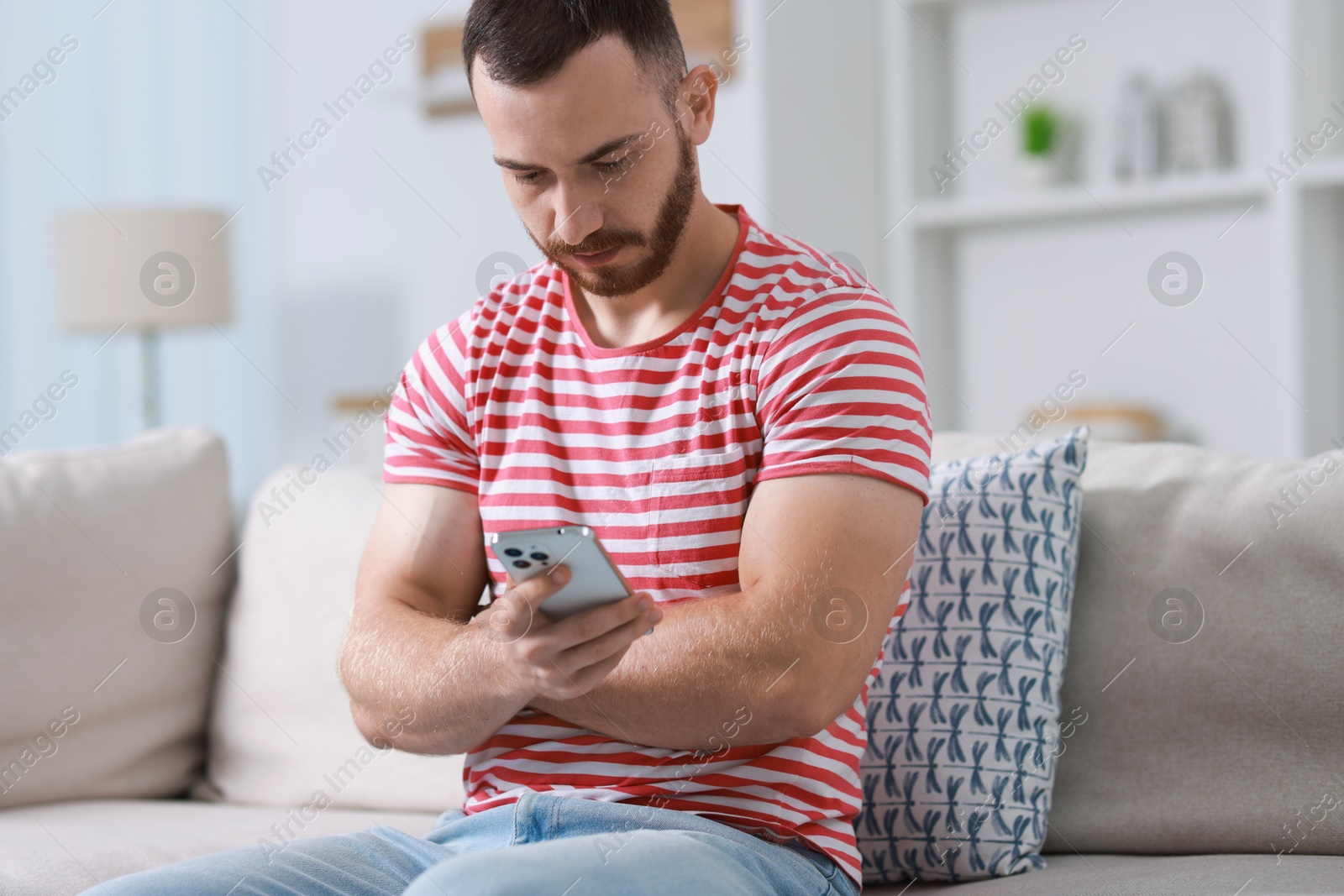 Photo of Handsome man using smartphone on sofa indoors