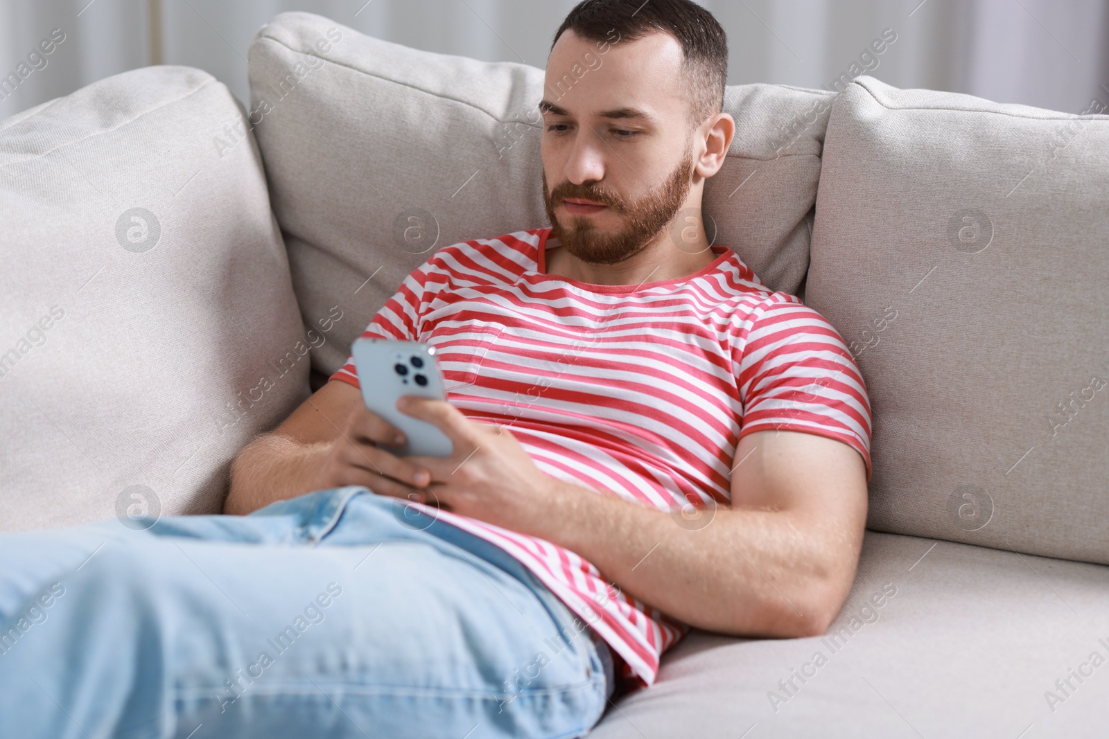 Photo of Handsome man using smartphone on sofa indoors