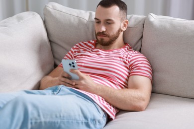 Handsome man using smartphone on sofa indoors