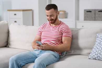 Photo of Handsome man using smartphone on sofa indoors