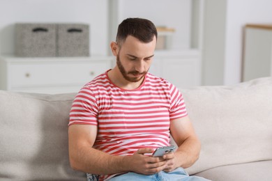 Handsome man using smartphone on sofa indoors