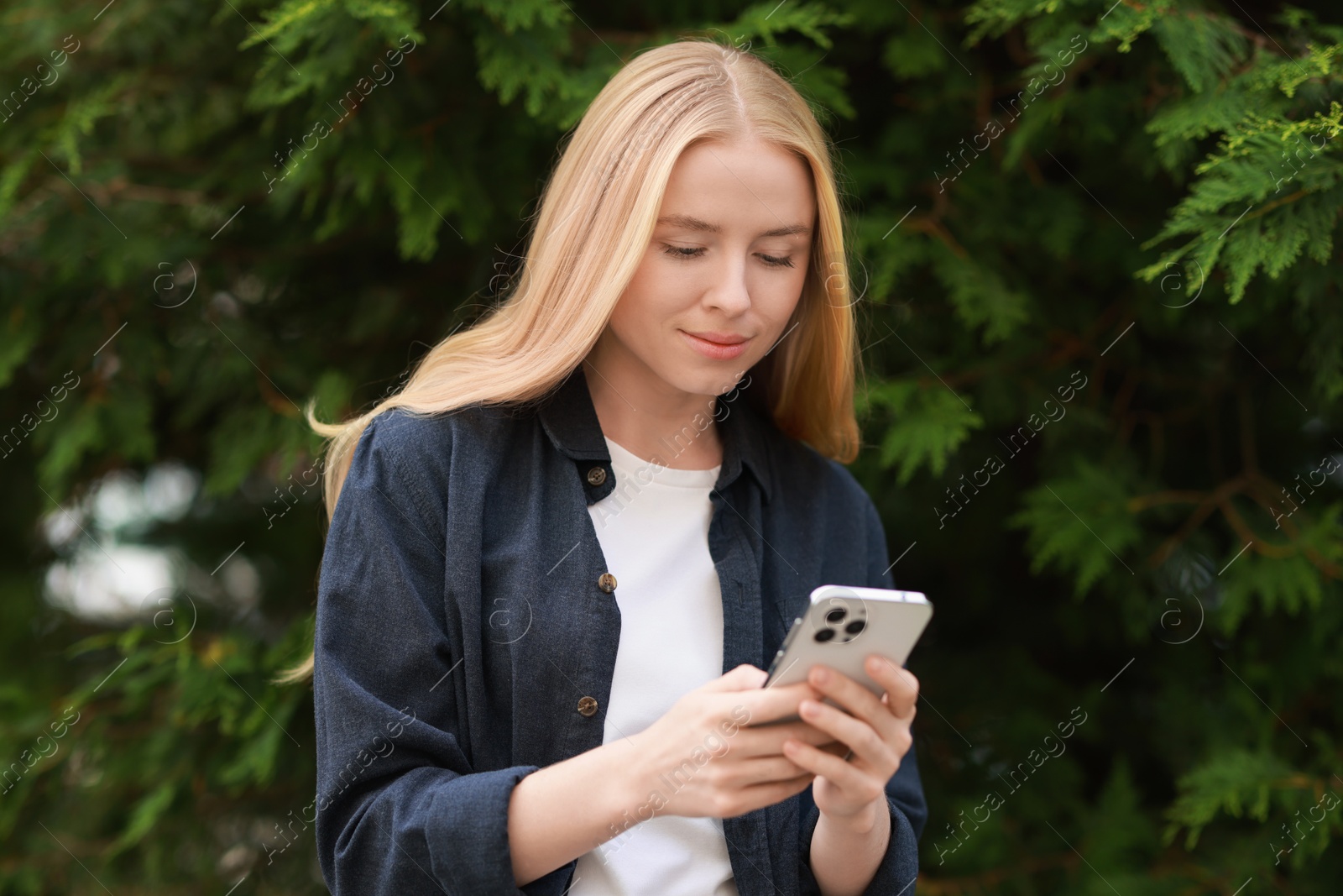 Photo of Beautiful woman using smartphone near tree outdoors