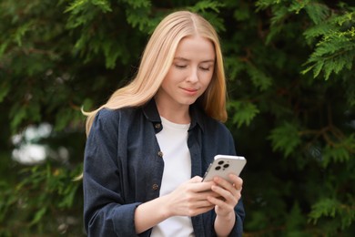 Beautiful woman using smartphone near tree outdoors