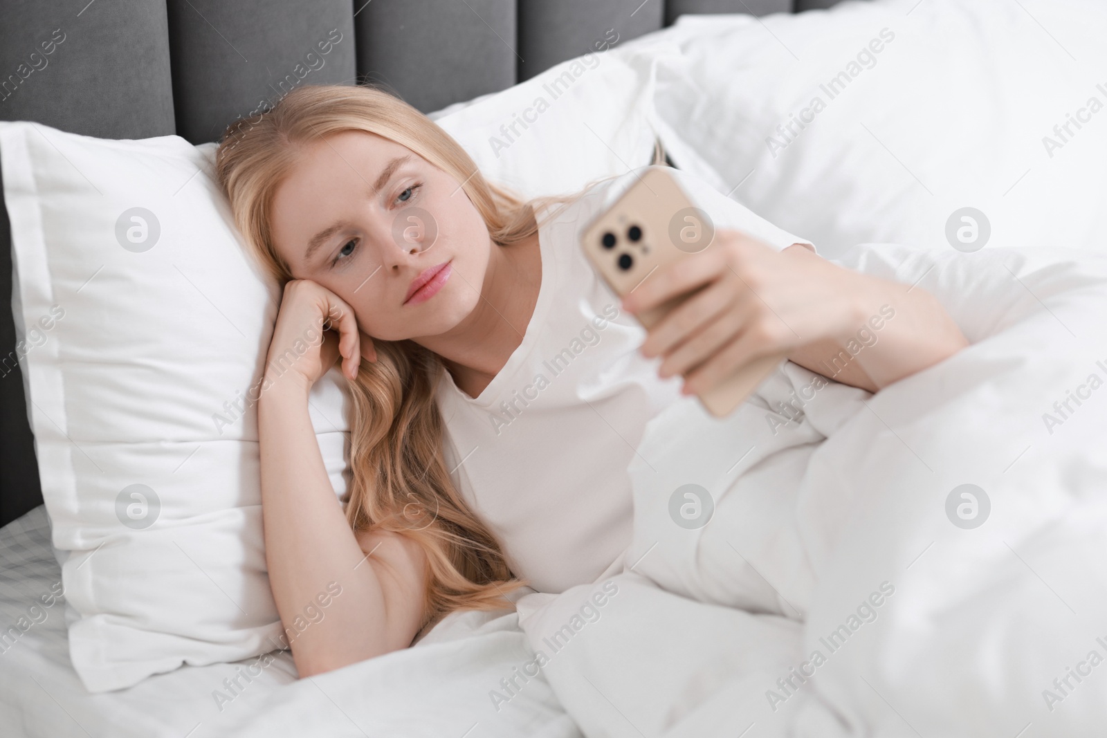 Photo of Beautiful woman looking at smartphone in bed