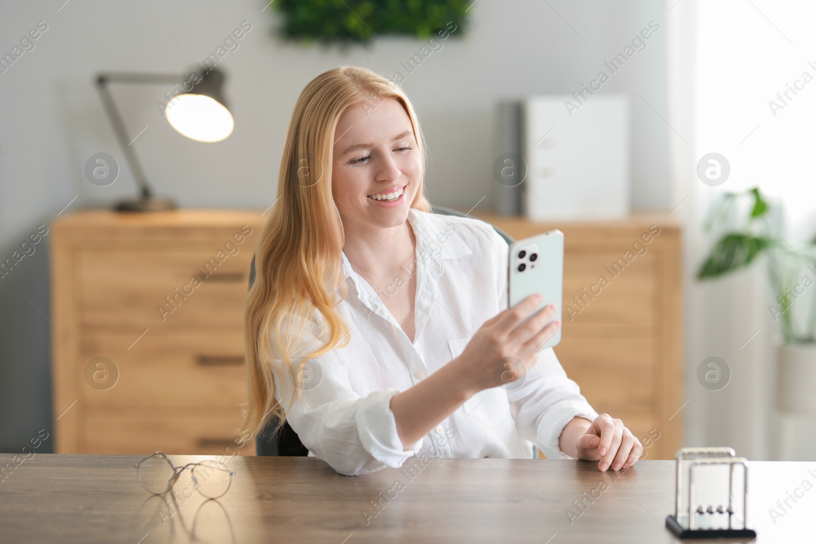 Photo of Smiling woman using smartphone at table in office